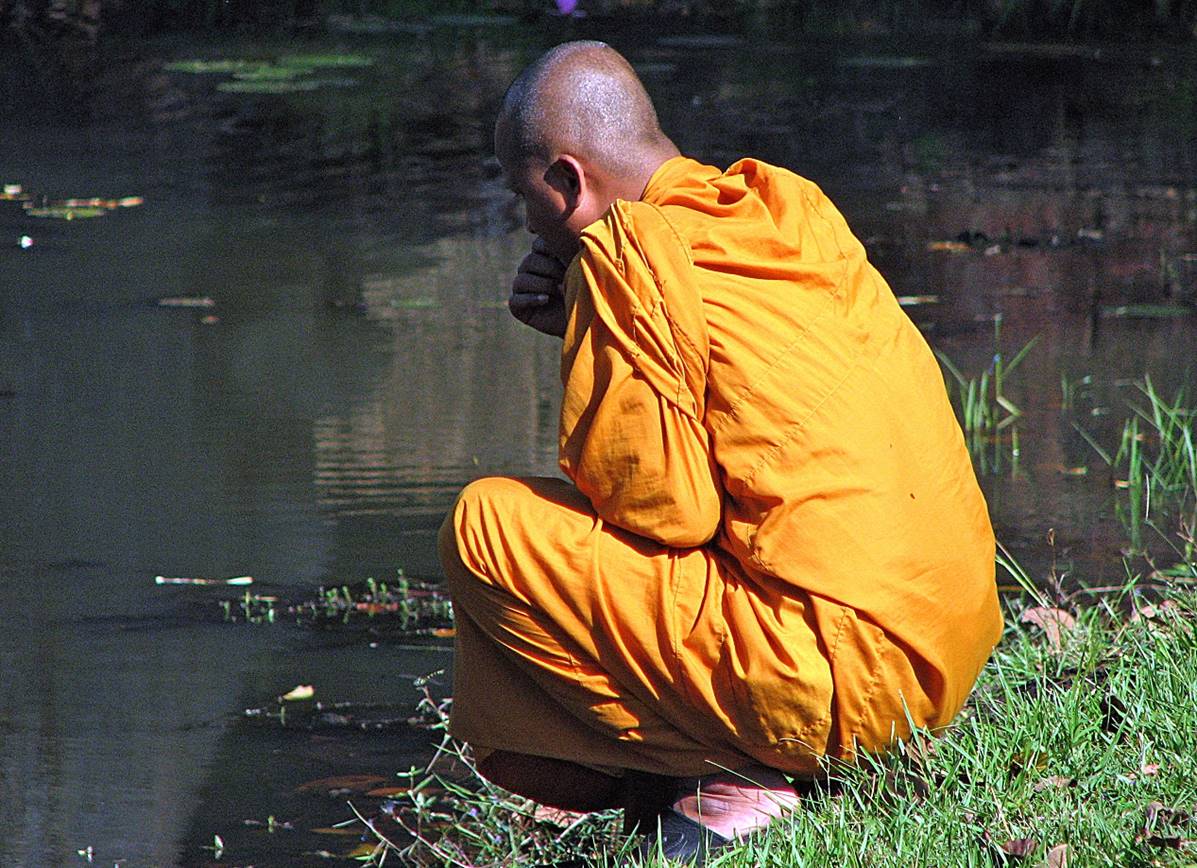 A monk kneeling on the edge of a river

Description automatically generated