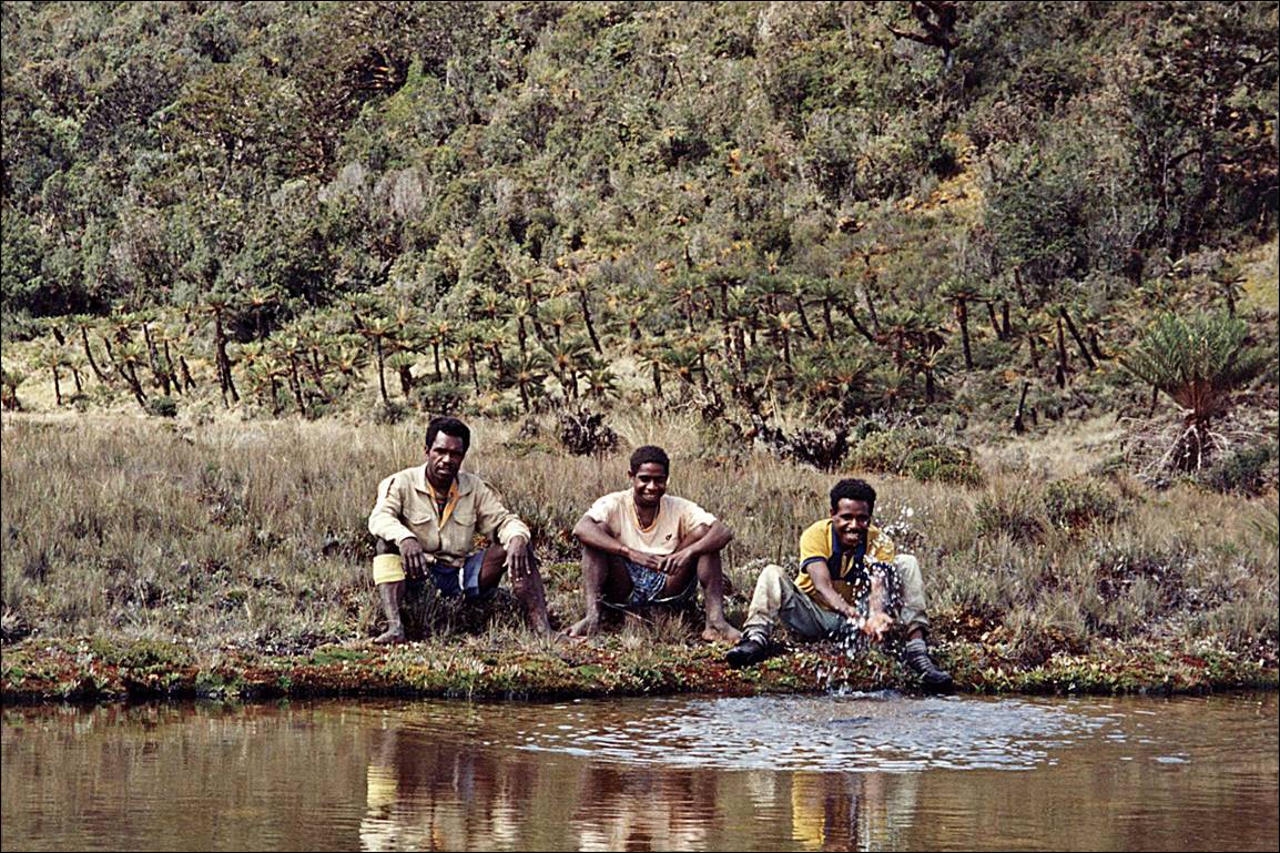A group of men sitting on the edge of a river

Description automatically generated