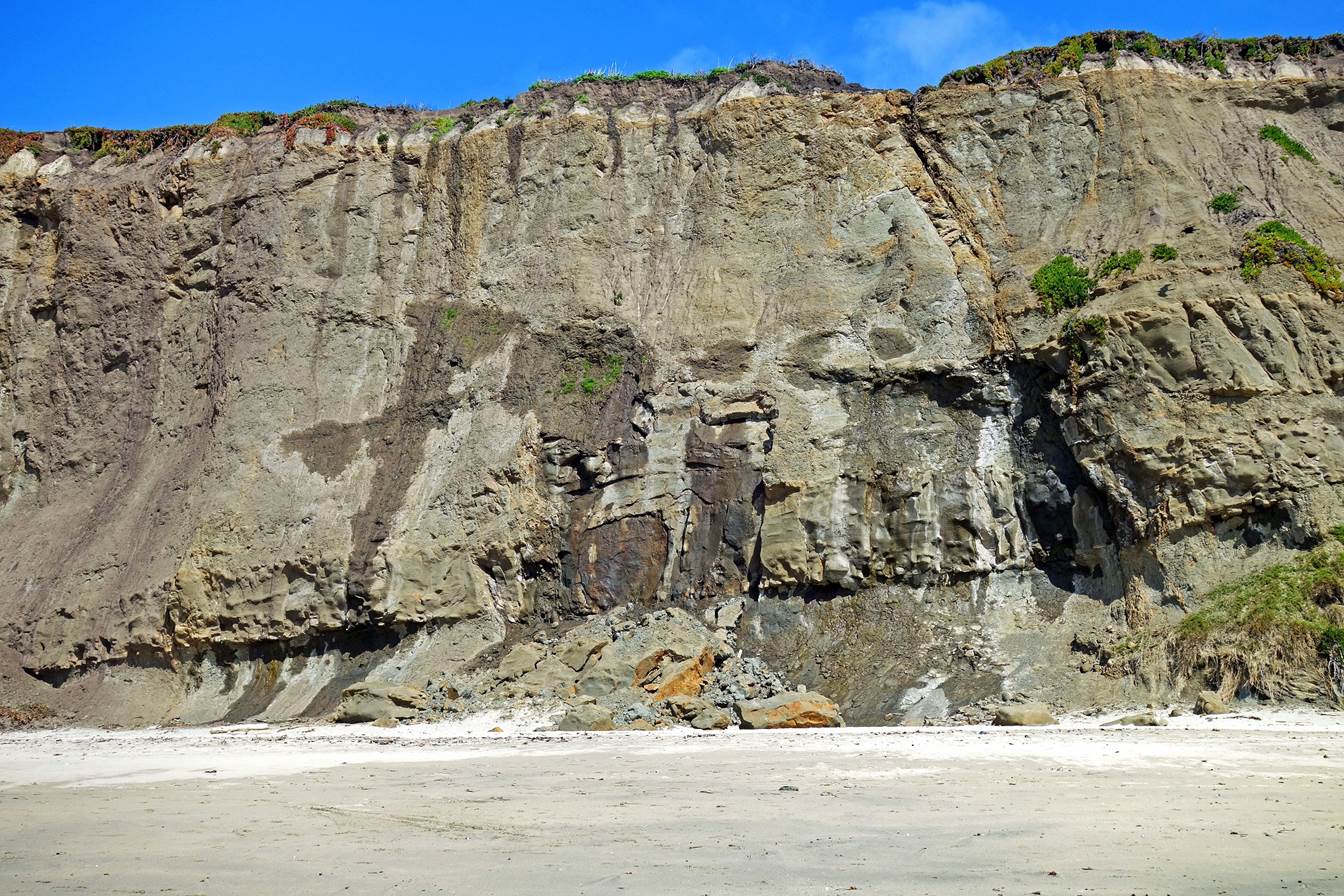 A large rock cliff with a sandy beach

Description automatically generated